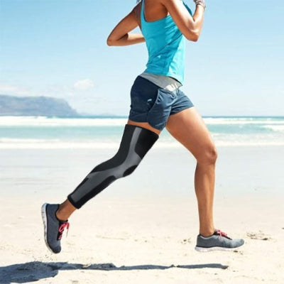 Une femme fait une redonnée à la plage avec ses manchons de compression - PulseFit aux genoux